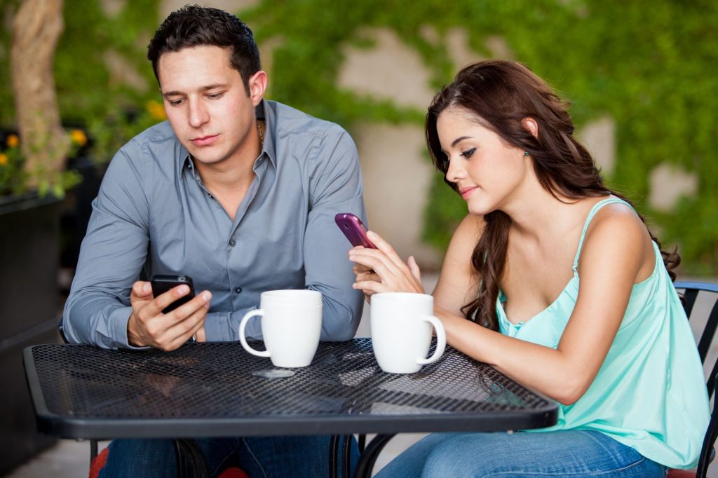 A couple on a coffee date staring at their smartphones.